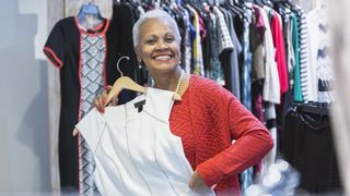 Es wird eine Dame gezeigt, welche sich über ein Kleid in einem Modegeschäft freut.