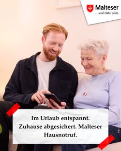 Ein junger Mann sitzt neben einer älteren Frau und erklärt ihr das Hausnotrufgerät.