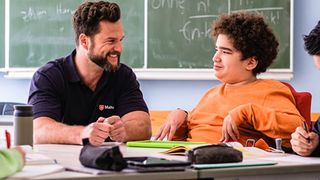 Malteser Schulbegleiter sitzt mit einem Jugendlichen im Rollstuhl im Klassenraum.