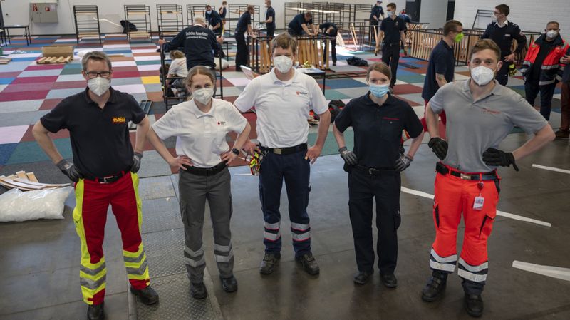 Mitarbeitende von ASB, DRK, den Johannitern und den Maltesern stehen nebeneinander in einer Halle.