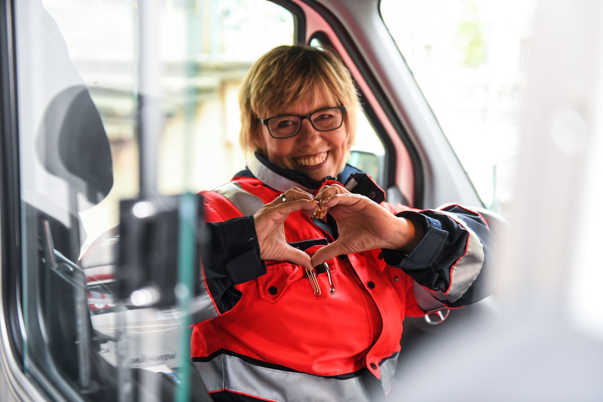 Malteser Mitarbeiterin im Herzenswunsch-Krankenwagen formt mit ihren Händen ein Herz.