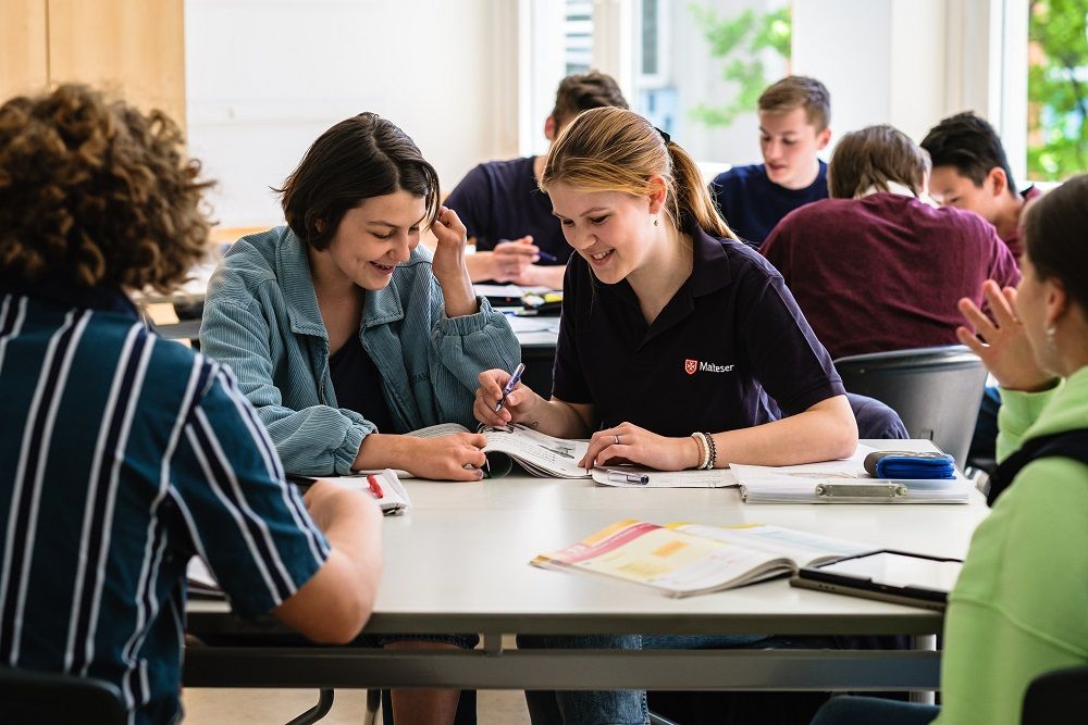 Eine Schulbegleiterin mit Schülern an einem Tisch