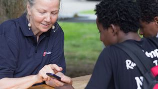 Eine Mitarbeiterin der Malteser Flüchtlingsbetreuung zeigt zwei Jungen etwas auf dem Handy.