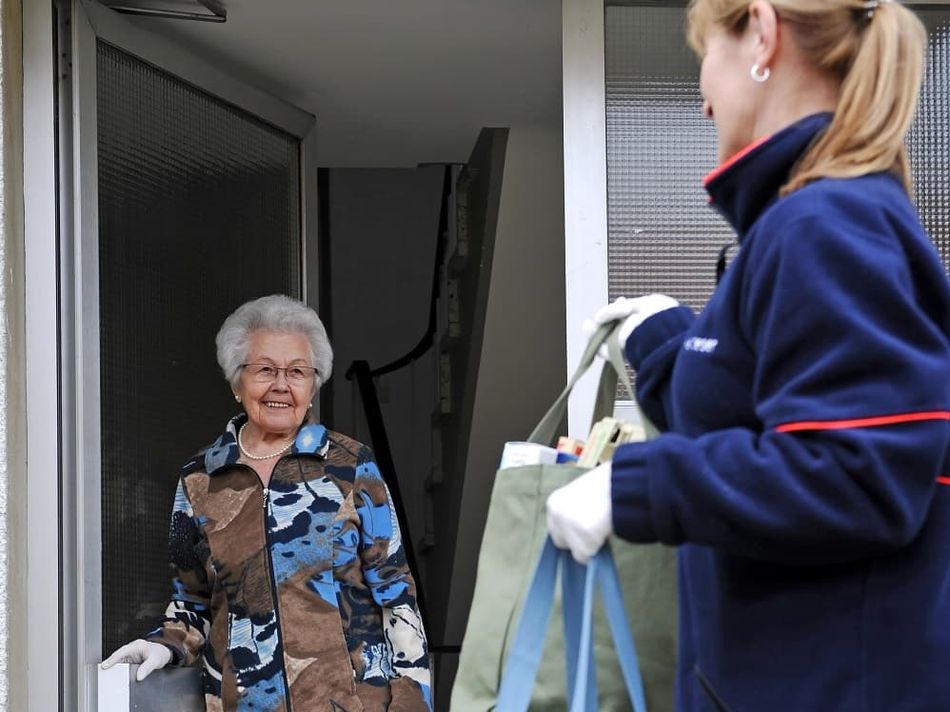 Eine Frau in einem blauen Pullover übergibt Einkäufe an eine ältere Frau.