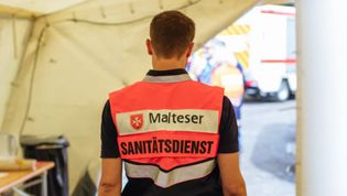 Malteser Sanitäter im Zelt von hinten fotografiert.