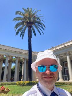 Dr. Stefan Tomaselli steht vor einer Palme und einem alten Gebäude mit Säulen