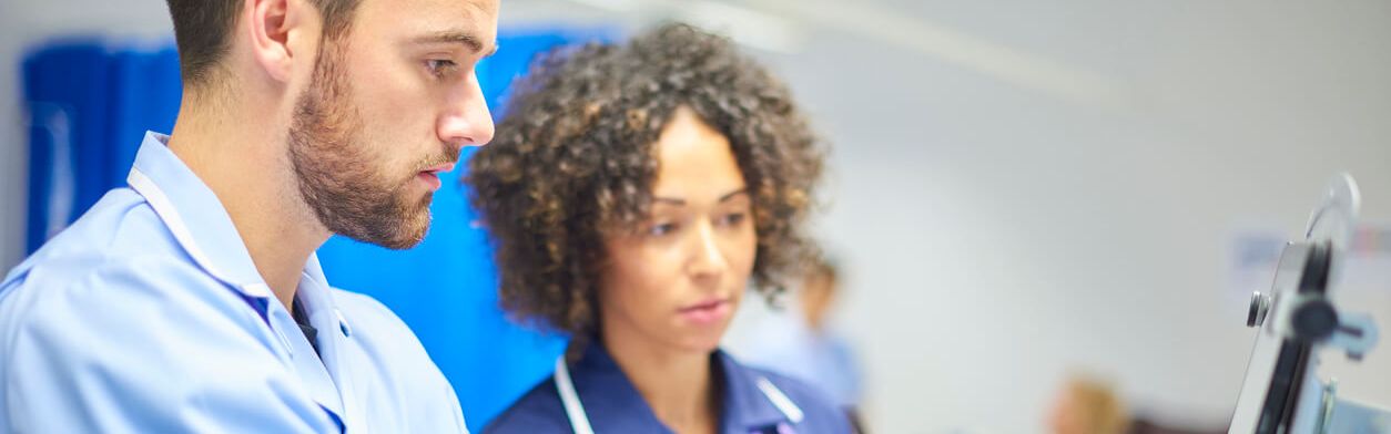 Unter Aufsicht einer Krankenpflegerin bedient ein Krankenpflegerazubi einen Klinikmonitor.