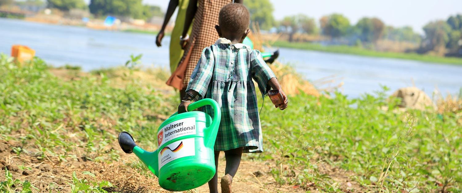 Ein Kind im Süd Sudan mit einer Gießkanne auf einem Feld