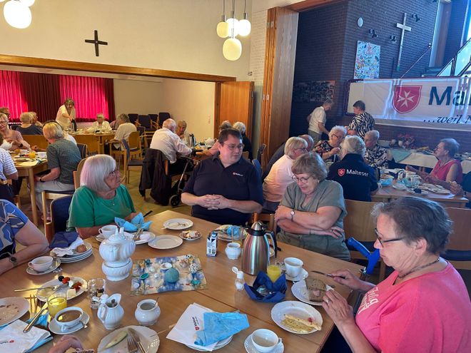 Panoramaaufnahme des Frühstücks, viele Menschen sitzen zusammen, reden und essen