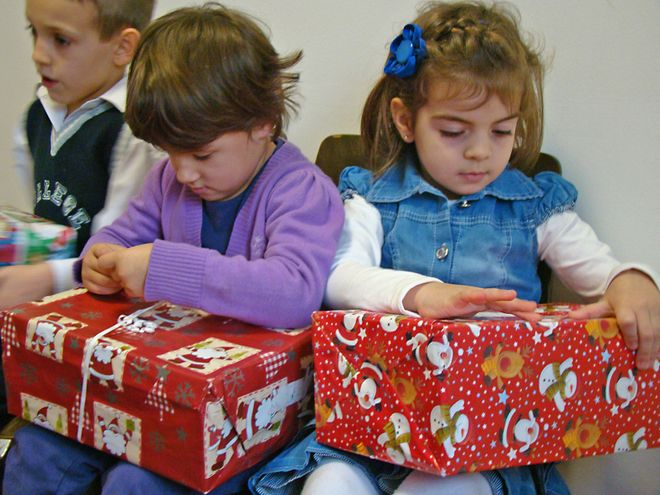 Zwei Kinder packen gemeinsam Weihnachtsgeschenke aus.