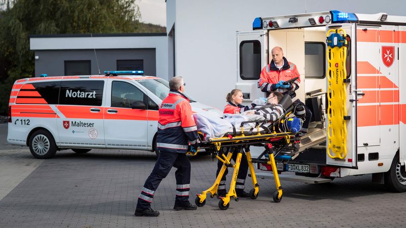 Drei Rettungsdienstsanitäter schieben Trage mit Patienten in den Rettungswagen