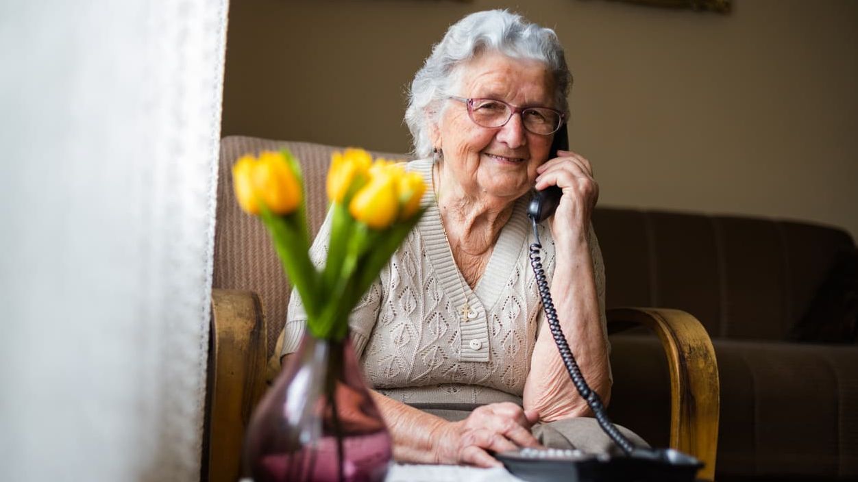 Eine alte Frau telefoniert in einem Wohnzimmer.