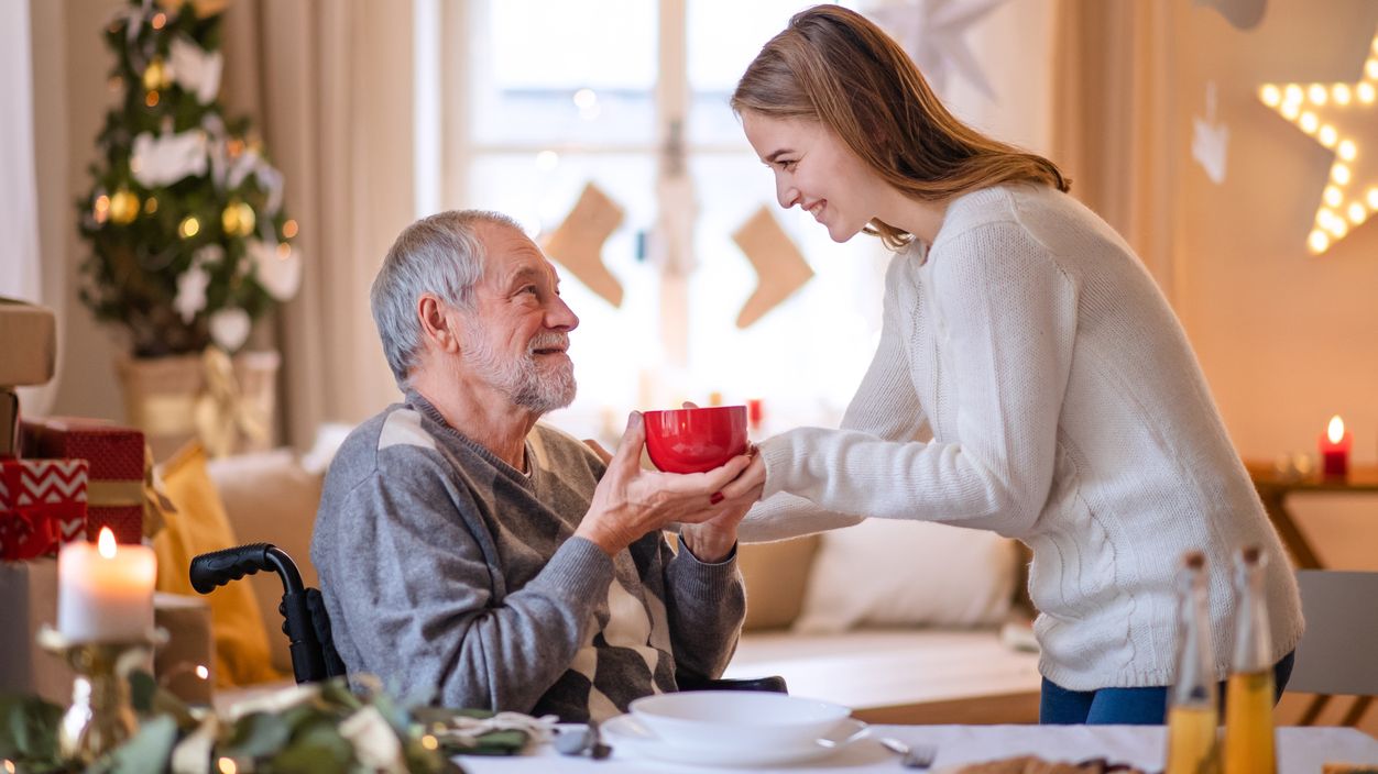 Eine junge Frau gibt einem älteren Mann im Rollstuhl einen Tasse Tee.