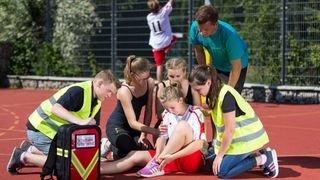 Malteser Schulsanitäter versorgen ein Mädchen, das sich beim Sport verletzt hat.