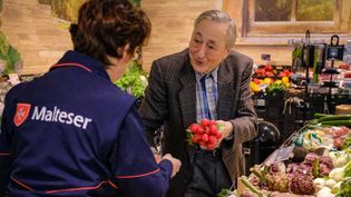 Malteser Helferin unterstützt einen älteren Mann beim Einkaufen im Supermarkt.