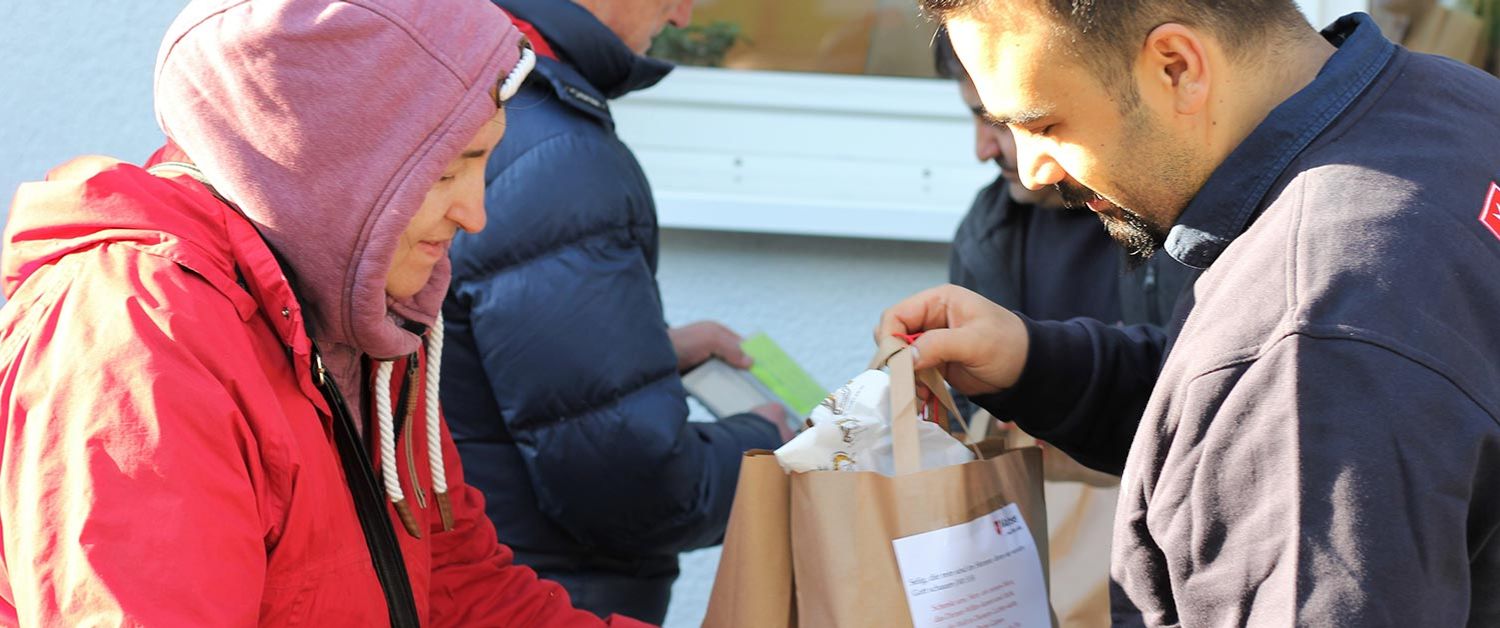 Ein Mitarbeiter der Malteser überreicht einer Frau in roter Winterjacke eine Papiertüte mit Lebensmitteln.