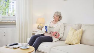 Ältere Dame auf der Couch mit Notruf-Armband