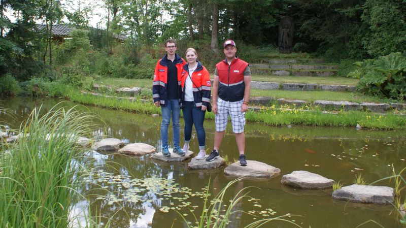 Drei junge Menschen auf Steinen in einem Teich.