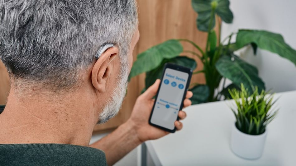 Mann mit Hörgerät schaut auf ein Smartphone