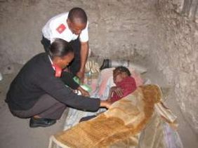 Two care workers examine a woman in her home.