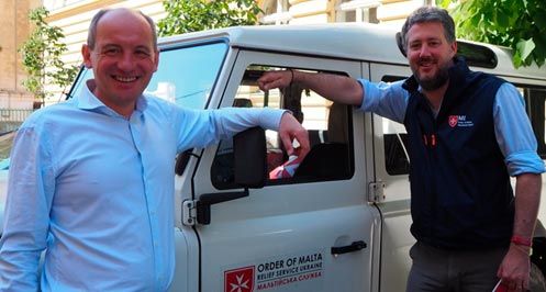 Zwei Männer sind an ein Auto mit Malteser-Aufdruck gelehnt