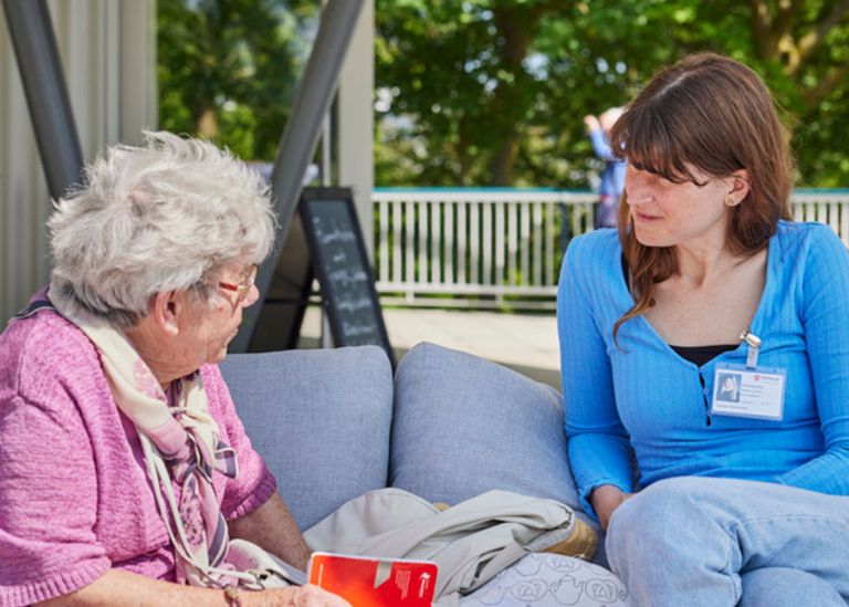 Eine ältere und eine junge Frau sitzen auf einer Couch im Freien und unterhalten sich.