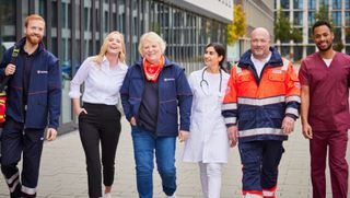 Malteser Mitarbeitende laufen gemeinsam durch den Innenhof eines Bürokomplexes.