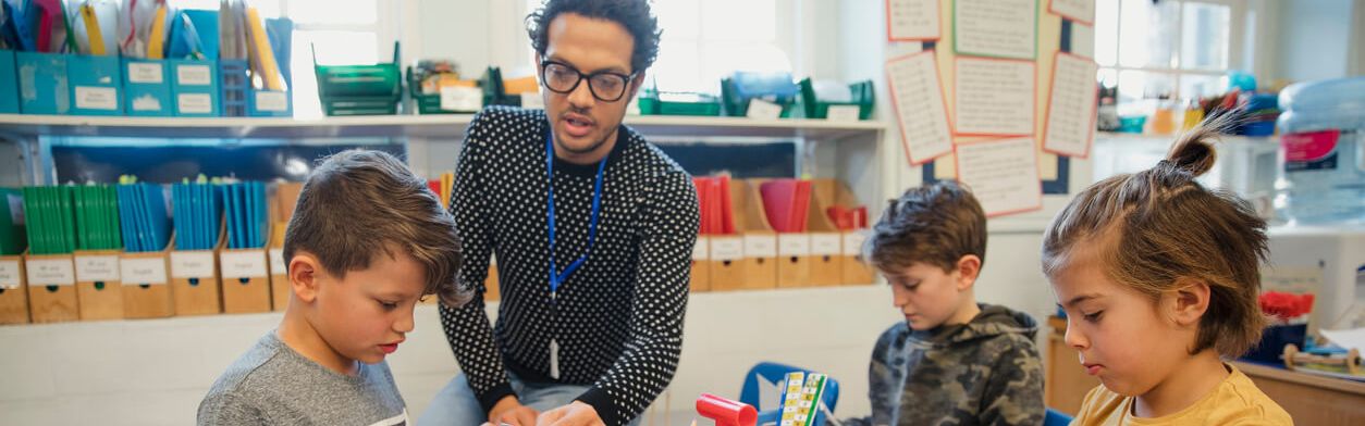 Junger Mann sitzt mit Schulkindern am Tisch und bastelt