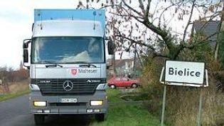 Weißer Lkw, der Hilfsgüter geladen hat, mit der Aufschrift Malteser neben dem Ortsschild von Bielice