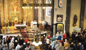 Ein Kircheninnenraum mit voll besetzten Bänken während einer Messe