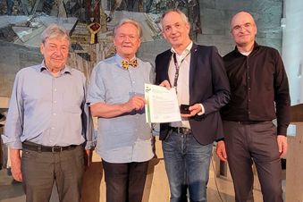 Vier Männer in einer Kirche, einer hält eine Urkunde und eine Skulptur.