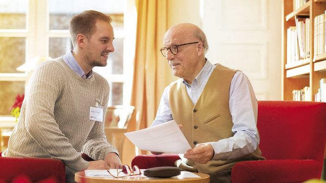 Zwei Männer beraten an einem Tisch sitzend zu einem Dokument.
