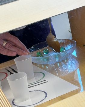 Ein Glasteller mit Murmeln, ein Löffel und zwei Becherchen. 