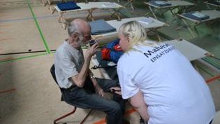 Eine Malteserin spricht in einer Turnhalle mit Feldbetten mit einem älteren Herren