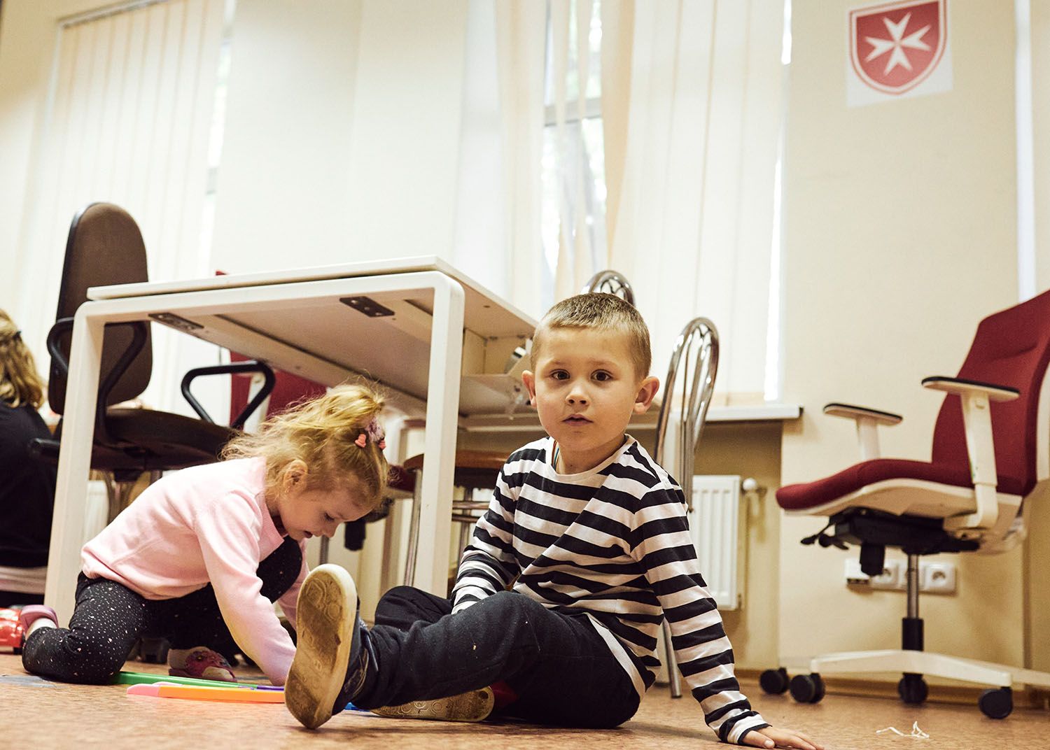 Zwei Kinder sitzen auf dem Boden vor einem Schreibtisch