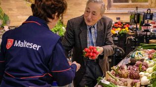 Malteser Helferin unterstützt einen älteren Mann beim Einkaufen im Supermarkt.
