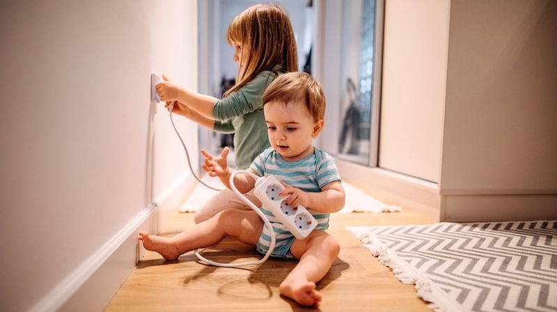 Zwei Kleinkinder spielen in einer Wohnung mit einer Steckdose.