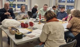 Mehrere Personen sitzen um einen Tisch und malen und basteln.