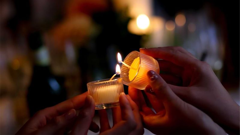 Ein Teelicht wird an einem weiteren Teelicht angezündet.