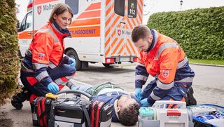 Eine Rettungssanitäterin und ein Rettungssanitäter versorgen einen Verletzten, der auf der Straße liegt. 