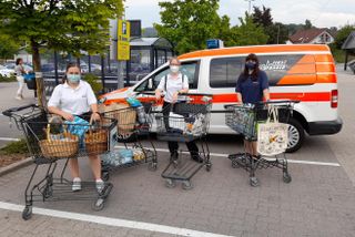 Drei Personen stehen mit gefüllten Einkaufswägen vor dem Malteser-Fahrzeug.