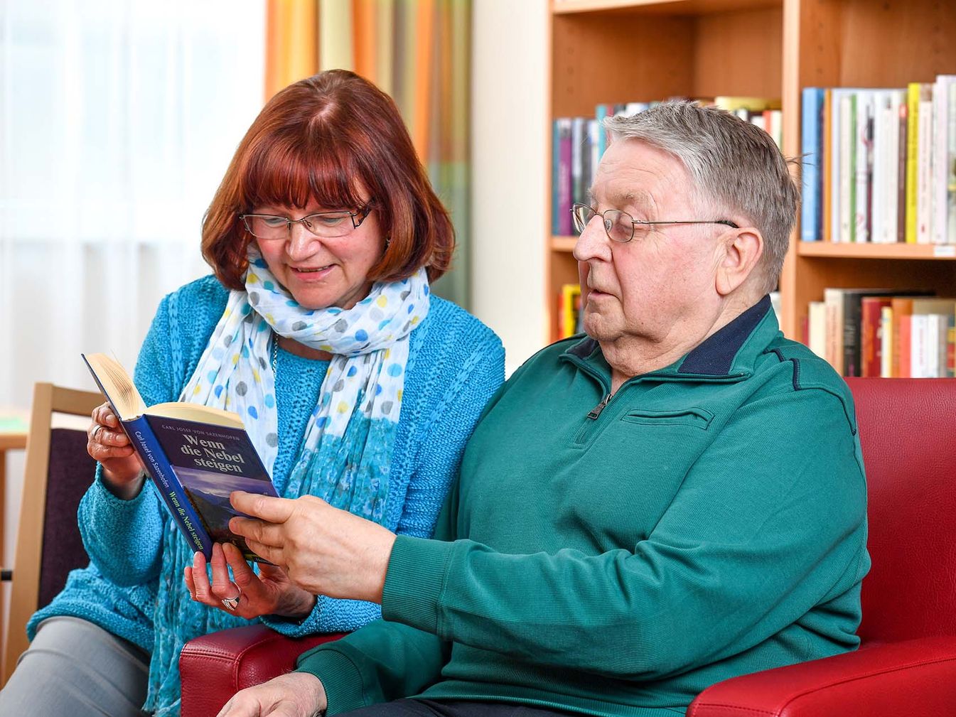 der Soziale Dienst und Bewohner lesen gemeinsam aus einem Buch 