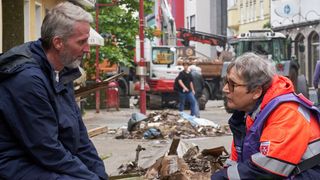 Malteser Mitarbeiterin in Einsatzkleidung im Gespräch mit einem Betroffenen der Flutkatastrophe.