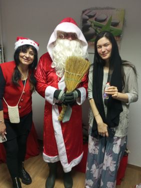 Drei Personen in weihnachtlicher Kleidung stehen zusammen und lächeln in die Kamera. In der Mitte steht der Weihnachtsmann und hält eine Rute in der Hand.