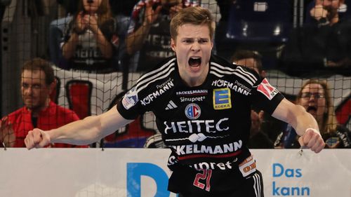 Handballspieler mit ausgestreckten Armen auf dem Spielfeld während eines Spiels.