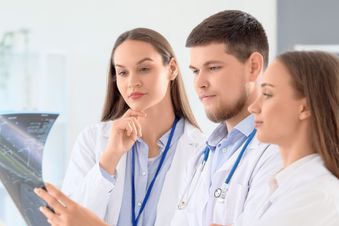 Drei Ärzte betrachten gemeinsam eine Röntgenaufnahme und diskutieren die Diagnose.