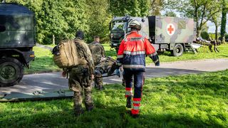Zwei Soldaten der Bundeswehr und ein Helfer des Malteser Rettungsdienstes transportieren einen Soldaten auf einer Trage.
