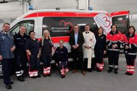 Viele Malteser in Dienstkleidung stehen neben Landrat Carsten Braun vor dem neuen Herzenswunschkrankenwagen