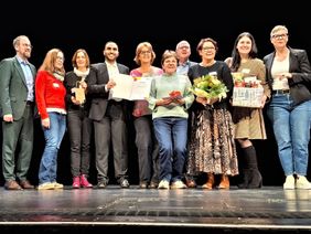 Zehn Personen stehen auf einer Bühne, zwei davon halten eine Urkunde.
