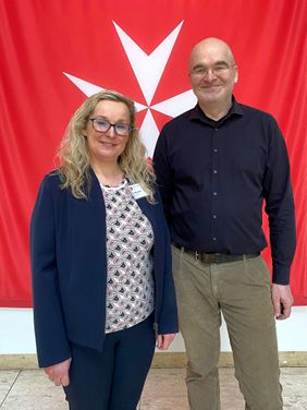 Eine Frau und ein Mann stehen vor einer roten Flagge.